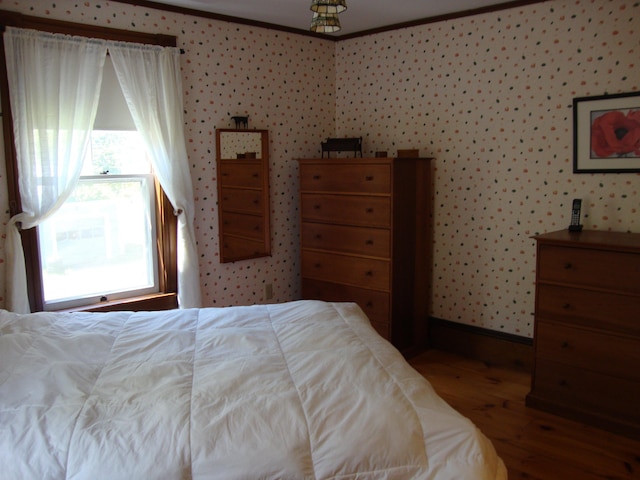 bedroom featuring wood finished floors, wallpapered walls, crown molding, and baseboards
