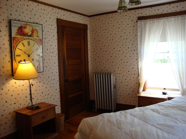 bedroom with radiator heating unit, ornamental molding, wood finished floors, and wallpapered walls