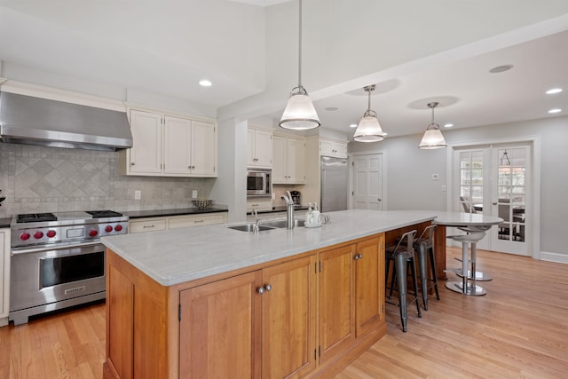 kitchen featuring built in appliances, wall chimney exhaust hood, a sink, light wood-style floors, and recessed lighting
