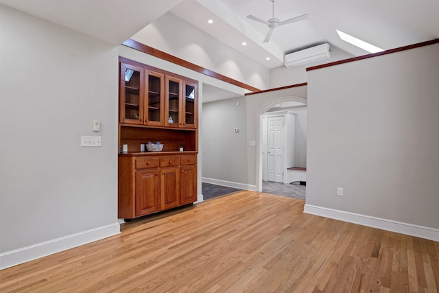 empty room featuring an AC wall unit, light wood-style flooring, arched walkways, baseboards, and high vaulted ceiling