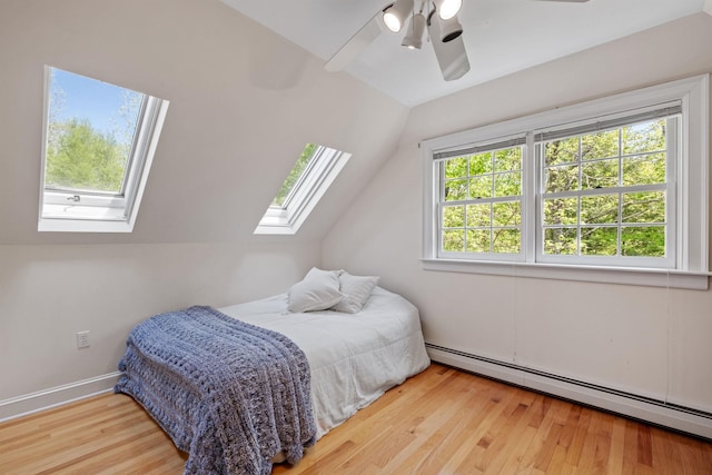 bedroom featuring baseboard heating, a skylight, lofted ceiling, wood finished floors, and a ceiling fan