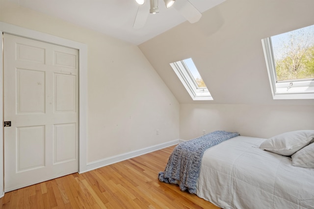 bedroom featuring a skylight, light wood-style flooring, vaulted ceiling, baseboards, and ceiling fan