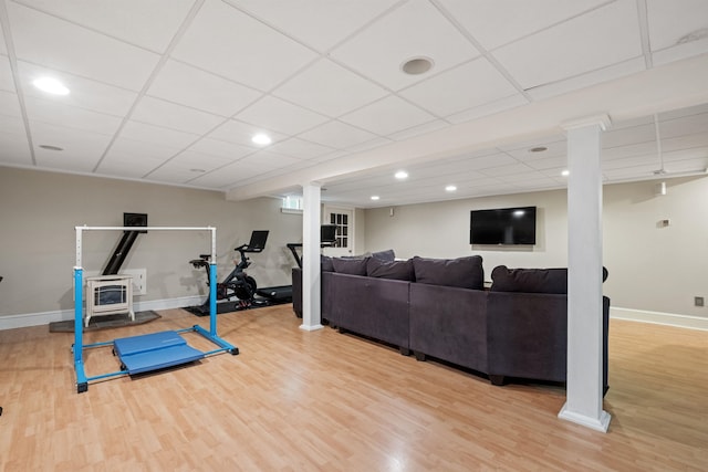 workout area featuring wood finished floors, baseboards, a wood stove, a paneled ceiling, and recessed lighting
