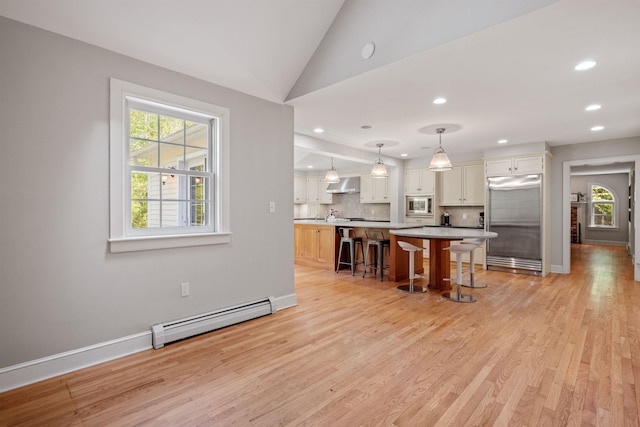 kitchen featuring built in appliances, a baseboard radiator, wall chimney exhaust hood, light wood-style floors, and a kitchen breakfast bar