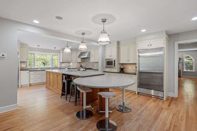 kitchen featuring built in appliances, wall chimney range hood, healthy amount of natural light, a sink, and recessed lighting