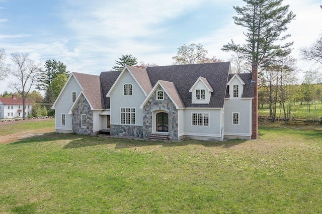 view of front of property featuring stone siding, a chimney, a front yard, and roof with shingles