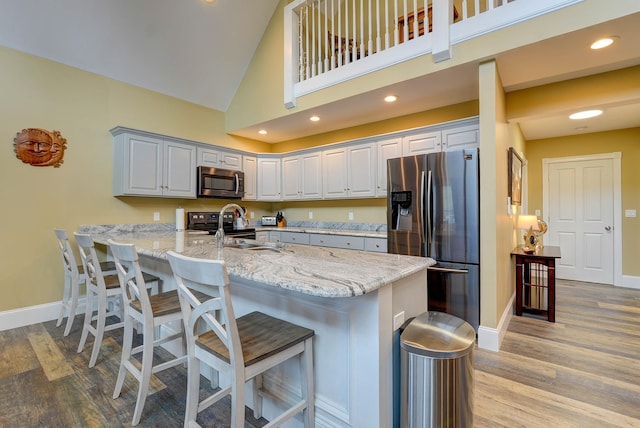kitchen with stainless steel appliances, a peninsula, baseboards, light wood finished floors, and high vaulted ceiling