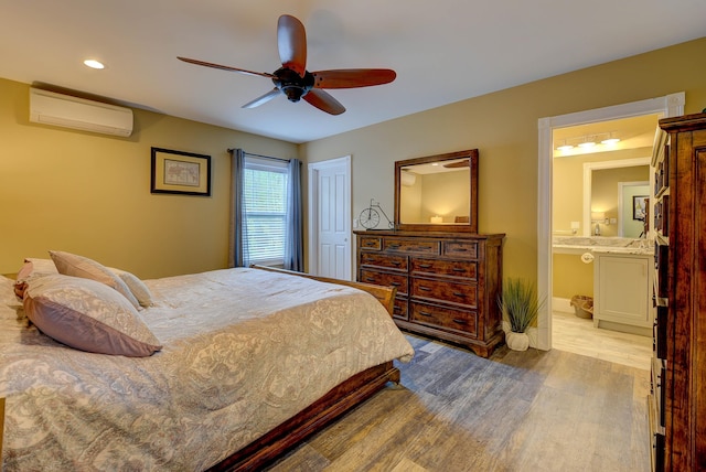 bedroom featuring a wall unit AC, wood finished floors, connected bathroom, recessed lighting, and a ceiling fan