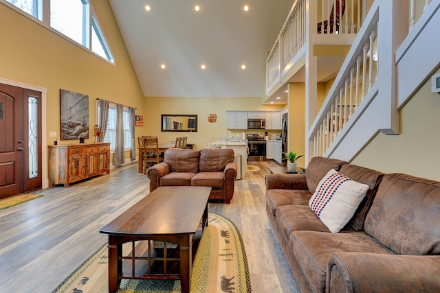 living room featuring high vaulted ceiling, light wood-style flooring, recessed lighting, and stairway