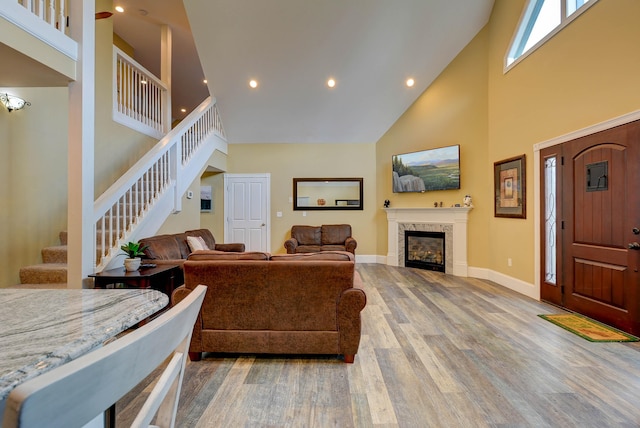 living room with a towering ceiling, wood finished floors, stairway, a tile fireplace, and baseboards