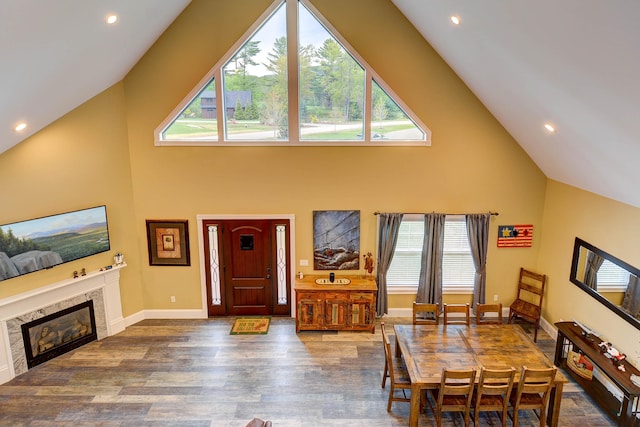 dining room with high vaulted ceiling, wood finished floors, healthy amount of natural light, a glass covered fireplace, and recessed lighting