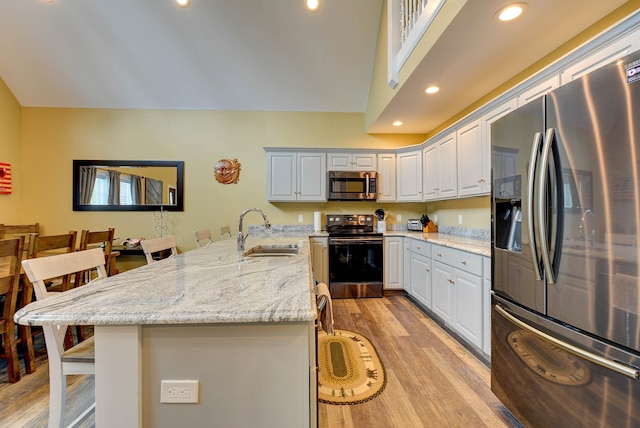 kitchen featuring appliances with stainless steel finishes, a sink, a kitchen breakfast bar, light wood-style flooring, and light stone counters