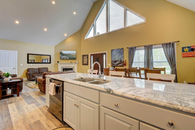 kitchen featuring a sink, high vaulted ceiling, dishwashing machine, a fireplace, and light wood-style floors