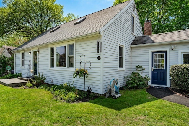 rear view of house with a lawn, a chimney, and roof with shingles