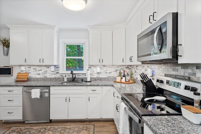 kitchen with appliances with stainless steel finishes, a sink, white cabinets, wood finished floors, and tasteful backsplash