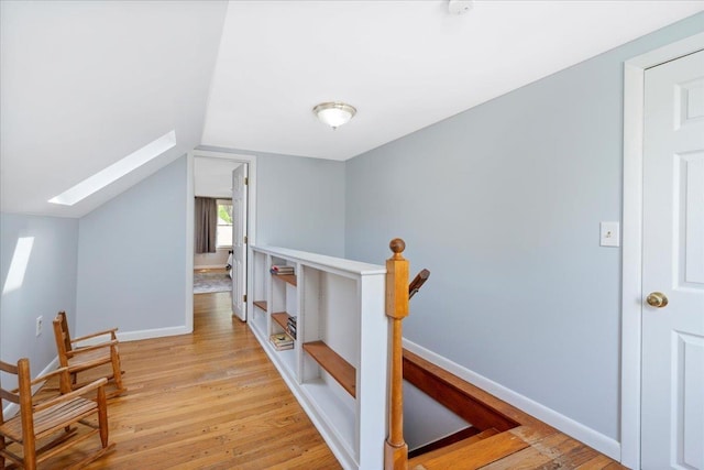 hallway with a skylight, an upstairs landing, light wood finished floors, lofted ceiling, and baseboards