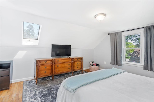 bedroom featuring a skylight, hardwood / wood-style floors, lofted ceiling, and baseboards