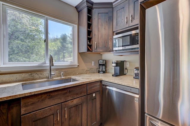 kitchen featuring stainless steel appliances, a sink, dark brown cabinets, and light stone counters