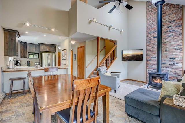 dining area with a wood stove, a high ceiling, ceiling fan, stairway, and stone finish flooring