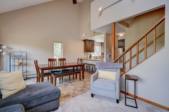 living area featuring a high ceiling, stairs, baseboards, light carpet, and baseboard heating