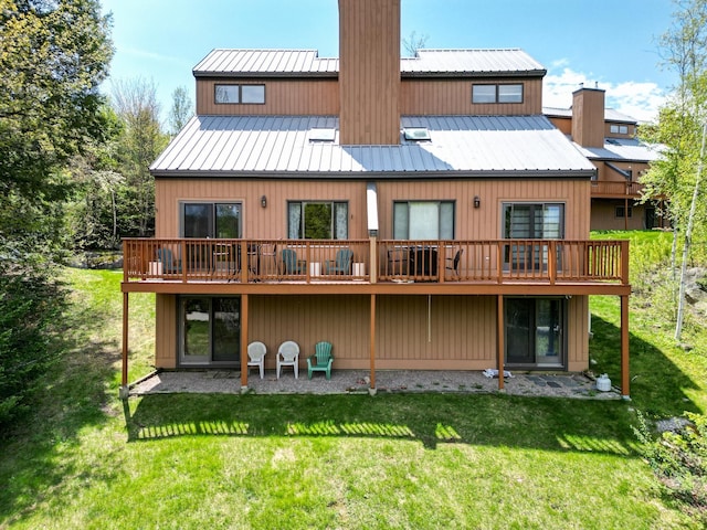 rear view of property featuring a chimney, a lawn, and a deck