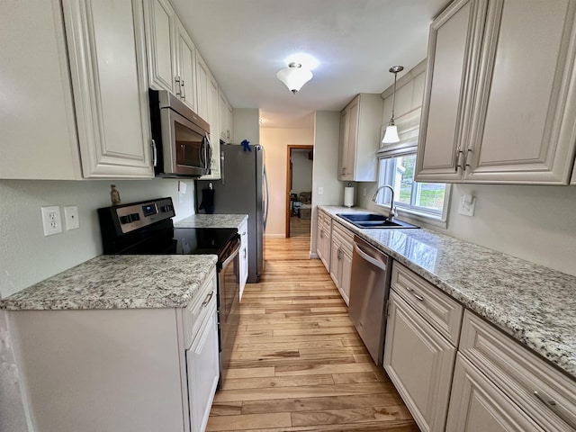 kitchen with stainless steel appliances, a sink, light wood-type flooring, decorative light fixtures, and light stone countertops