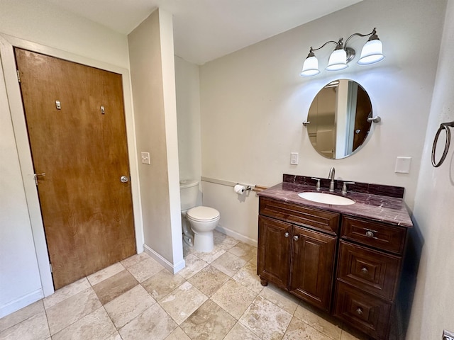 bathroom featuring toilet, vanity, baseboards, and stone finish flooring