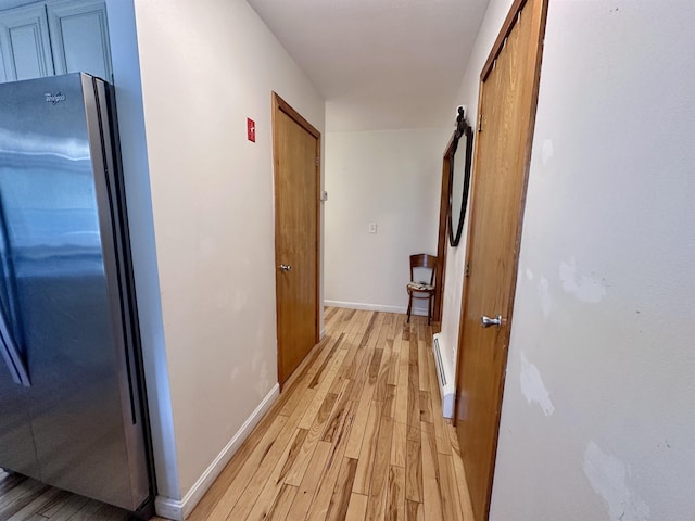 corridor featuring baseboard heating, light wood-type flooring, and baseboards