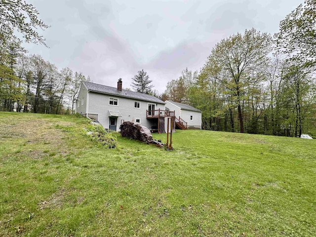 rear view of property featuring a chimney, stairway, a deck, and a lawn