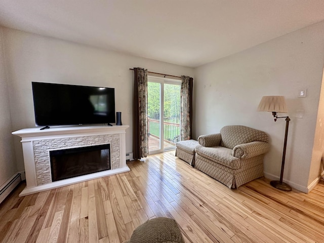 living area with wood finished floors, baseboard heating, a fireplace, and baseboards