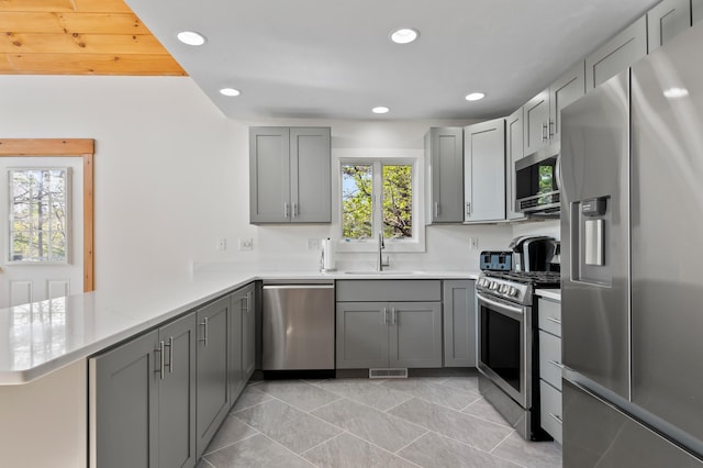kitchen with appliances with stainless steel finishes, a sink, gray cabinetry, a peninsula, and light countertops