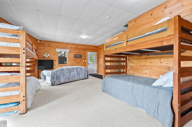 carpeted bedroom featuring wooden walls and a paneled ceiling