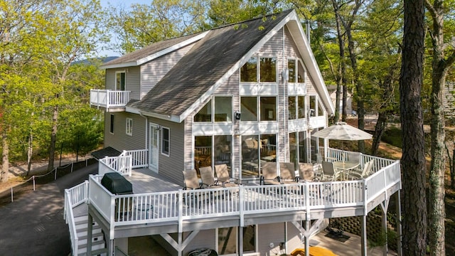 back of property with roof with shingles, a wooden deck, outdoor dining space, stairs, and a balcony