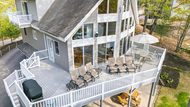 back of property with a wooden deck, outdoor dining area, and roof with shingles