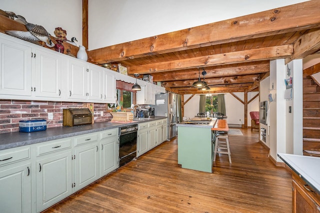 kitchen with appliances with stainless steel finishes, dark countertops, dark wood-style flooring, white cabinets, and a center island
