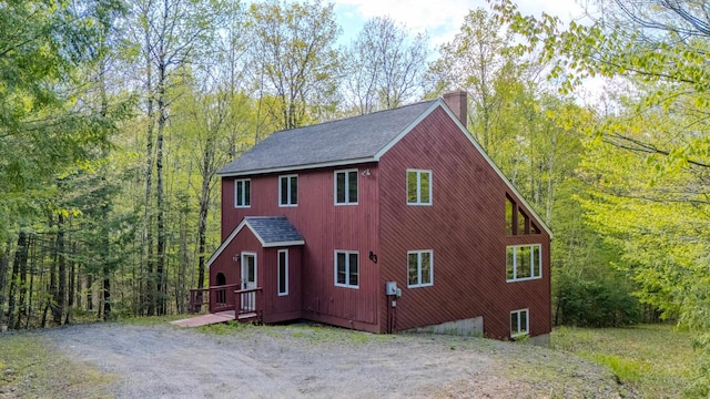view of property exterior with a chimney, a shingled roof, and a wooded view