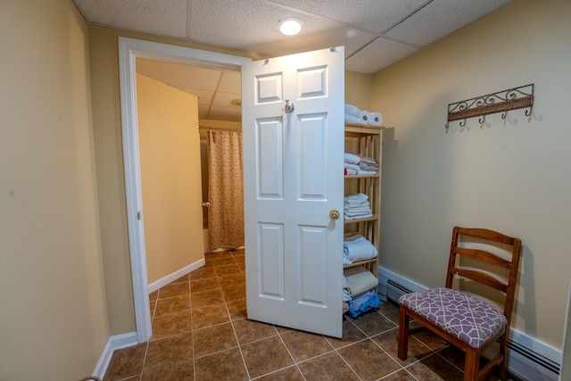 interior space featuring a baseboard radiator, a drop ceiling, dark tile patterned flooring, and baseboards