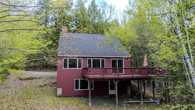 back of property featuring a deck, roof with shingles, and a chimney