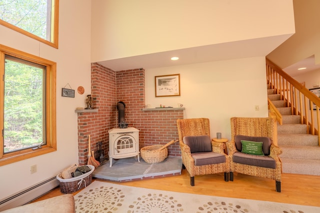 living area featuring healthy amount of natural light, wood finished floors, a wood stove, stairs, and a high ceiling