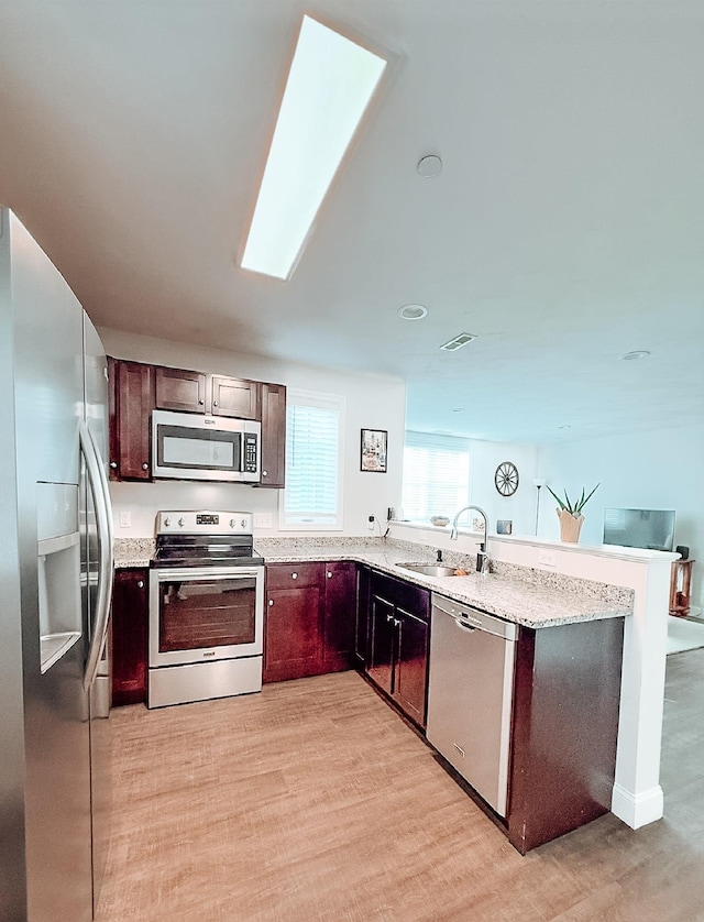 29 Bennett St, Nashua, NH 03064 - kitchen with stainless steel appliances, a sink, a peninsula, light stone counters, and light wood-style flooring