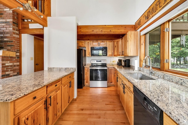 kitchen featuring black appliances, a sink, light wood-style flooring, light stone counters, and a towering ceiling