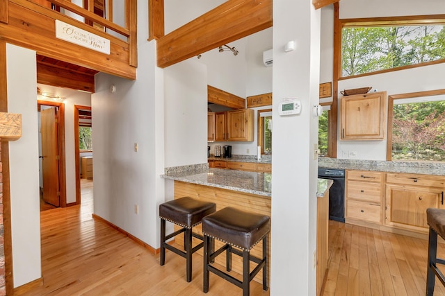 kitchen with a high ceiling, light wood finished floors, black dishwasher, a kitchen breakfast bar, and light stone counters