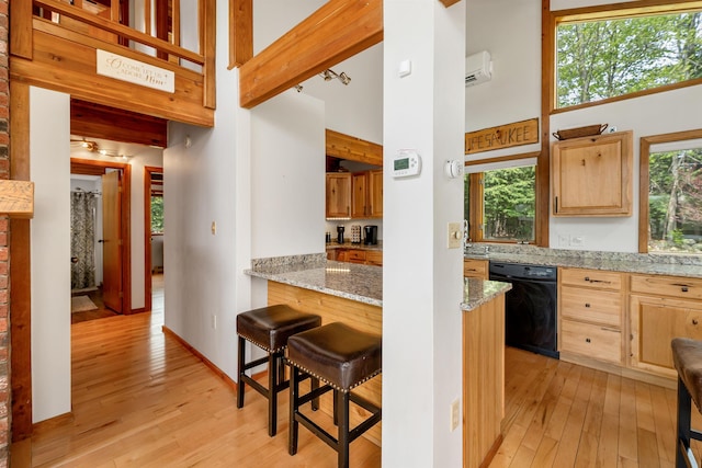 kitchen featuring black dishwasher, light wood-style floors, a towering ceiling, light brown cabinetry, and light stone counters