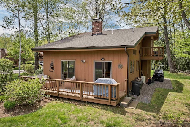 rear view of house featuring a chimney, roof with shingles, a wooden deck, and a lawn