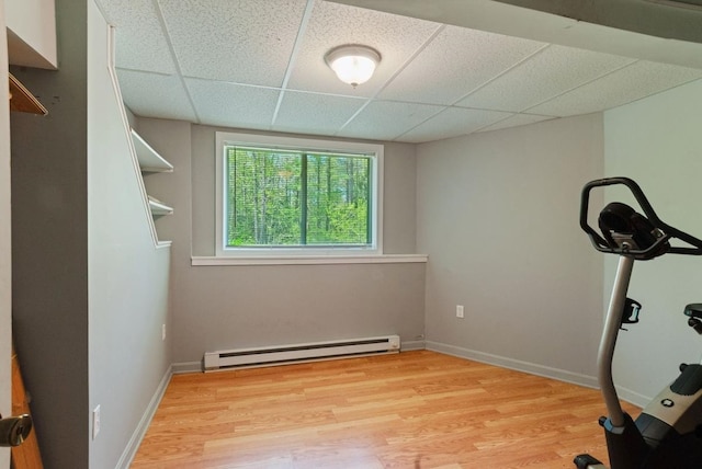 exercise area with baseboard heating, light wood-style flooring, a paneled ceiling, and baseboards