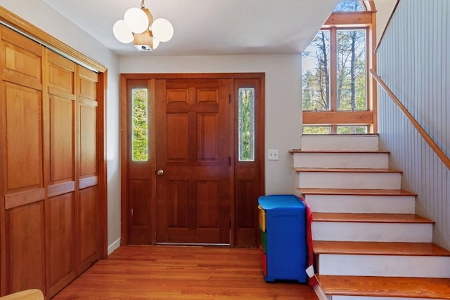 entryway featuring stairs, light wood-style floors, a chandelier, and healthy amount of natural light