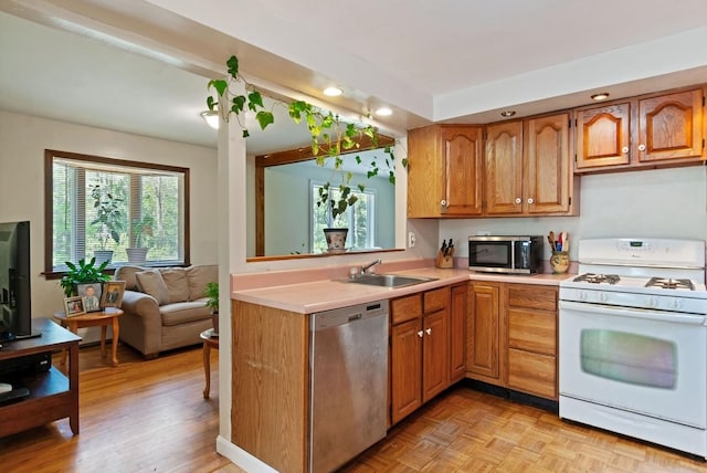 kitchen featuring appliances with stainless steel finishes, light countertops, a sink, recessed lighting, and brown cabinets