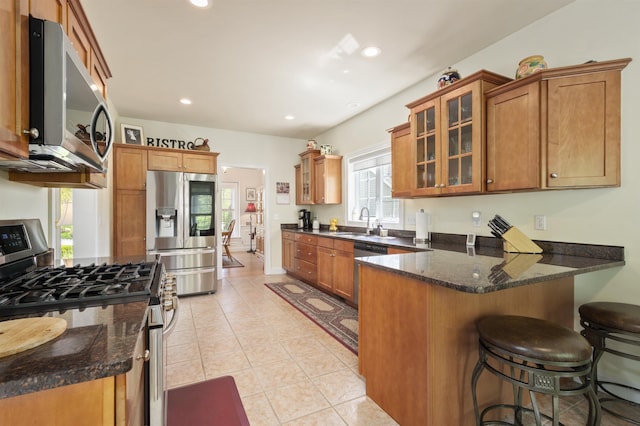 kitchen with stainless steel appliances, a peninsula, a sink, brown cabinets, and glass insert cabinets