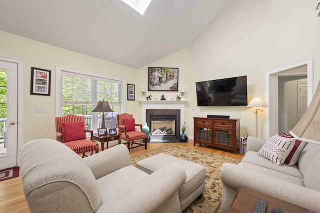 living room featuring wood finished floors, a fireplace with flush hearth, high vaulted ceiling, and a skylight