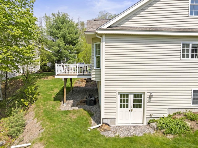view of side of property with a wooden deck, a yard, and roof with shingles